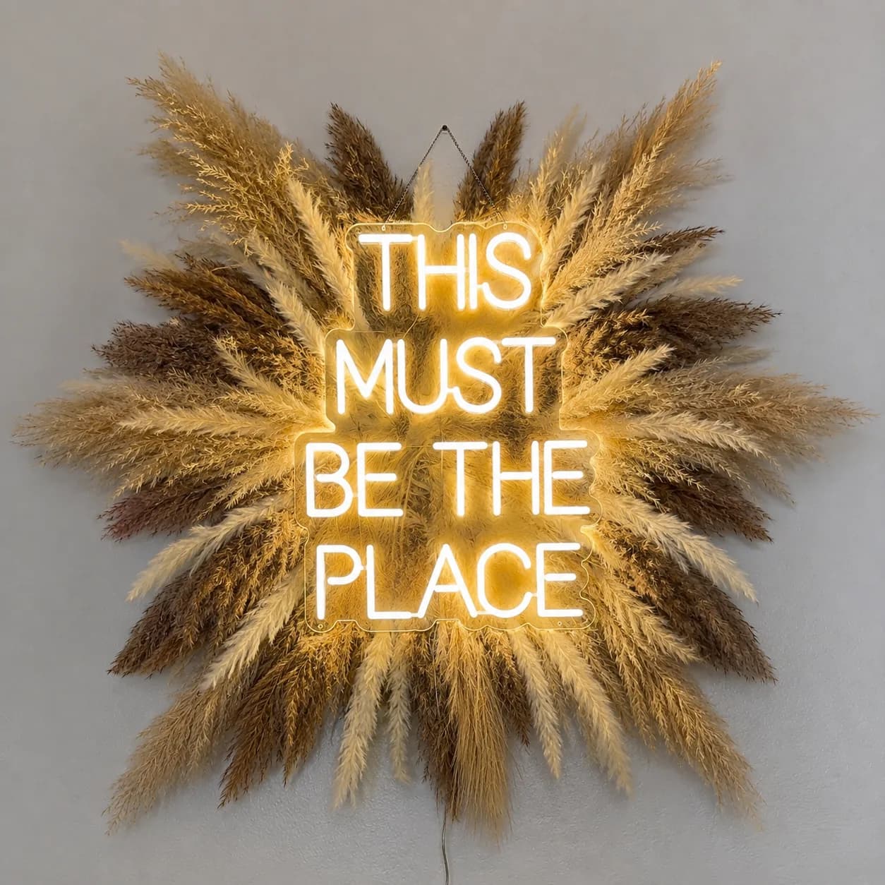 A neon 'This Must Be The Place' sign framed by pampas grass in the studio